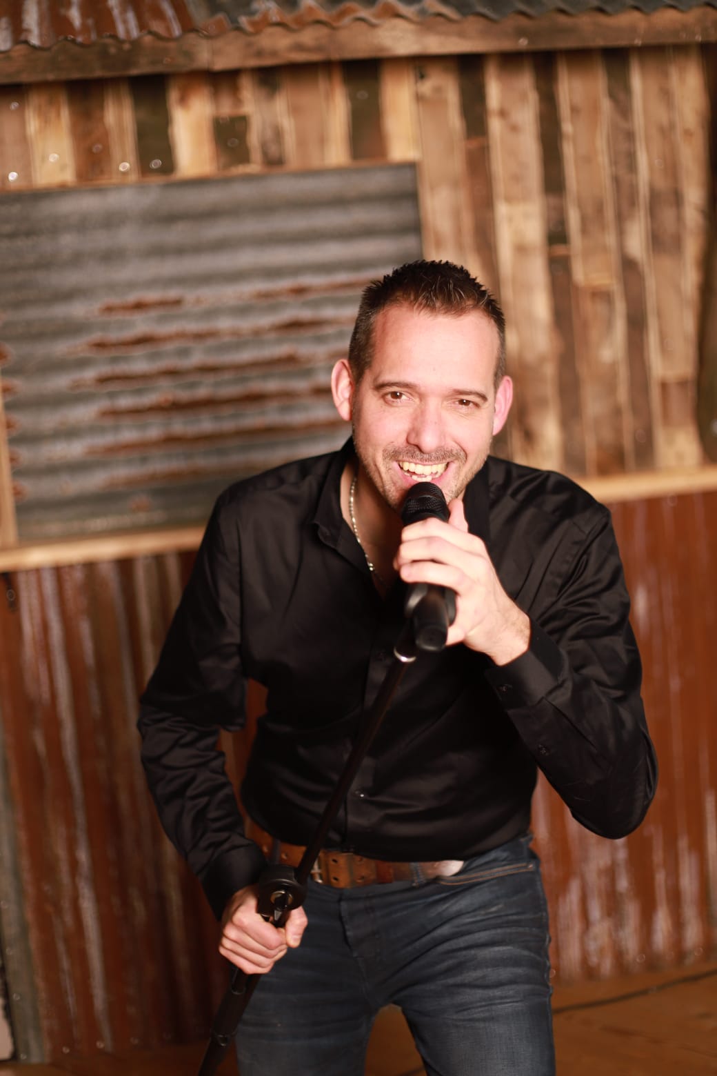 Erik van der Veen tijdens een optreden met microfoon in zwart overhemd